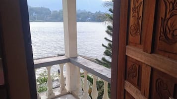 A view from a balcony with a wooden railing and a white balustrade, overlooking a body of water and distant mountains.