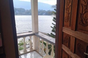 Vista desde un balcón con barandilla de madera y balaustrada blanca, con vista a una masa de agua y montañas distantes.