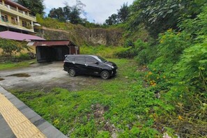 A black SUV parked on a grassy area with a building in the background. - Sibayak Guest house (Samosir Regency)