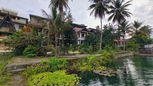 A riverside view with buildings, palm trees, and a small dock. - Sibayak Guest house (Samosir Regency)