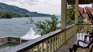 A balcony with a view of a lake and mountains, a white tent, and a covered area with chairs. - Sibayak Guest house (Samosir Regency)