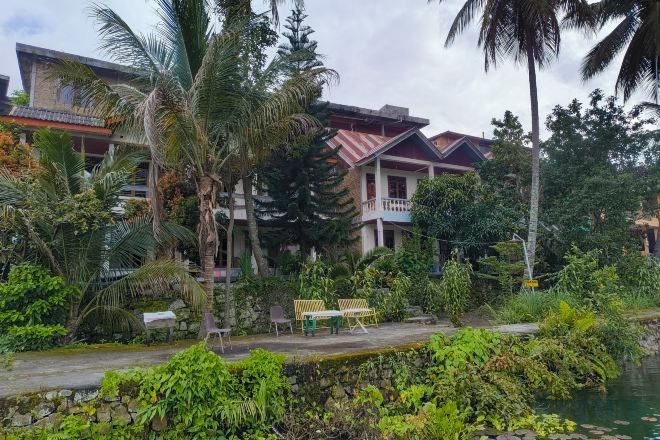 A residential building with a balcony, surrounded by lush greenery and a small water body.