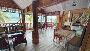 A wooden-floored room with a table and chairs, a 'Welcome' sign, and a view of palm trees and water. - Sibayak Guest house (Samosir Regency)