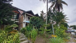 A residential building with a balcony, surrounded by lush greenery and a palm tree. - Sibayak Guest house (Samosir Regency)