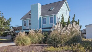 Une maison à deux étages, à la façade bleu clair, avec un toit gris et une petite fenêtre au deuxième étage.