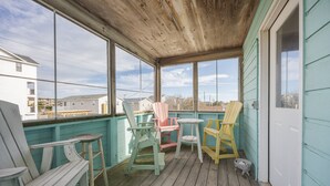 Une véranda couverte avec un plancher en bois, des murs de couleur turquoise et de grandes fenêtres offrant une vue sur les maisons voisines.