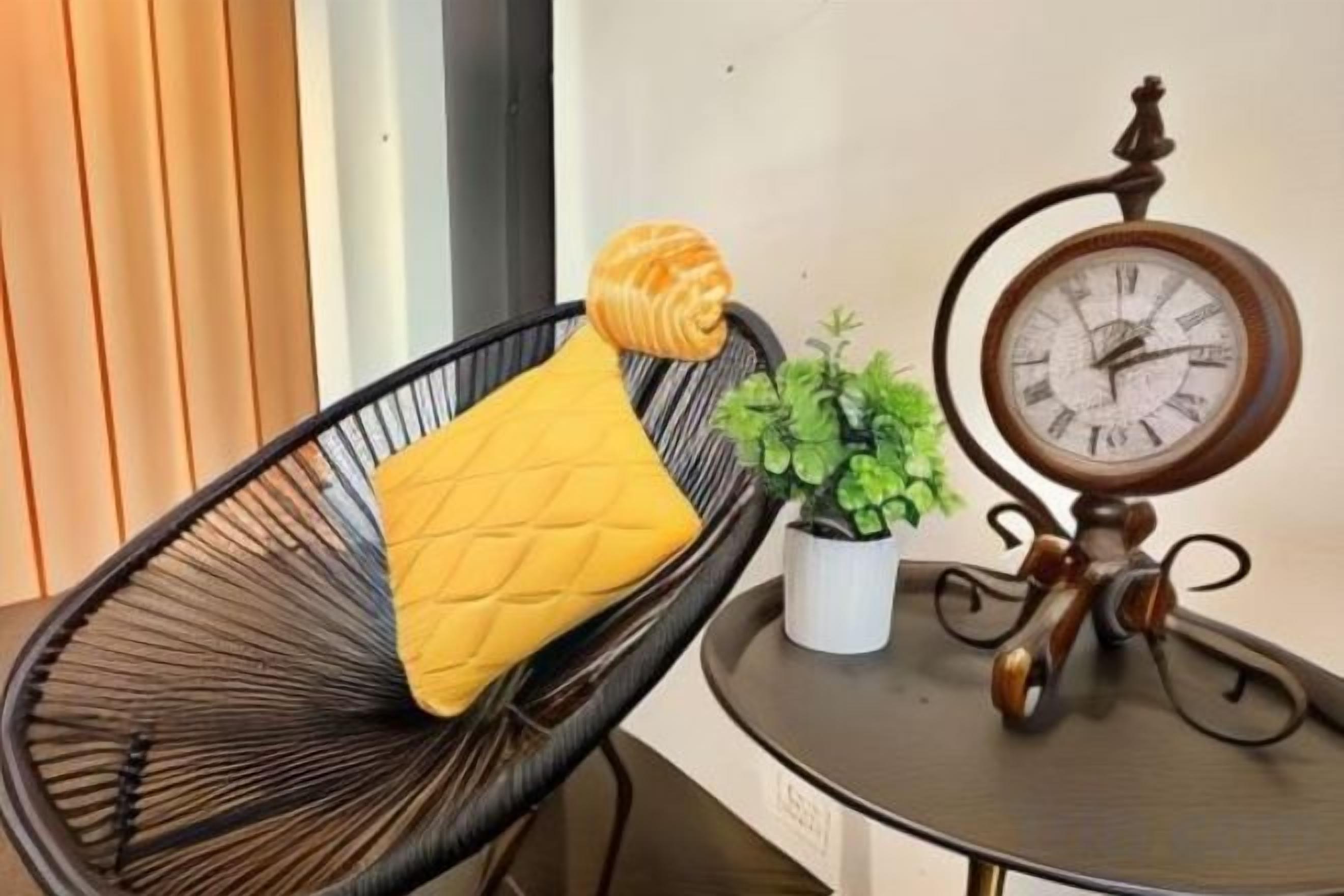 A black wire chair with a yellow cushion and a small potted plant beside it.