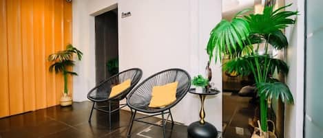 Un vestíbulo con dos sillones de mimbre negro, una mesita redonda y una planta en maceta.