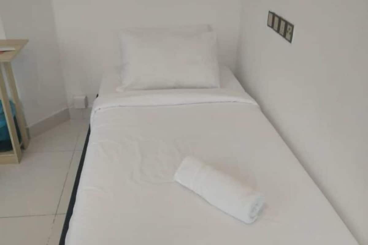 A single bed with white bedding, a small bedside table, and a wall-mounted light switch.