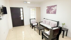 Uma sala de estar com sofá, cadeiras, mesa de centro e televisão.