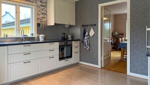 A modern kitchen with white cabinets, a black countertop, and a wooden floor. There is a window with a view of a house outside. - 2 bedroom beautiful home in Påskallavik (Påskallavik)