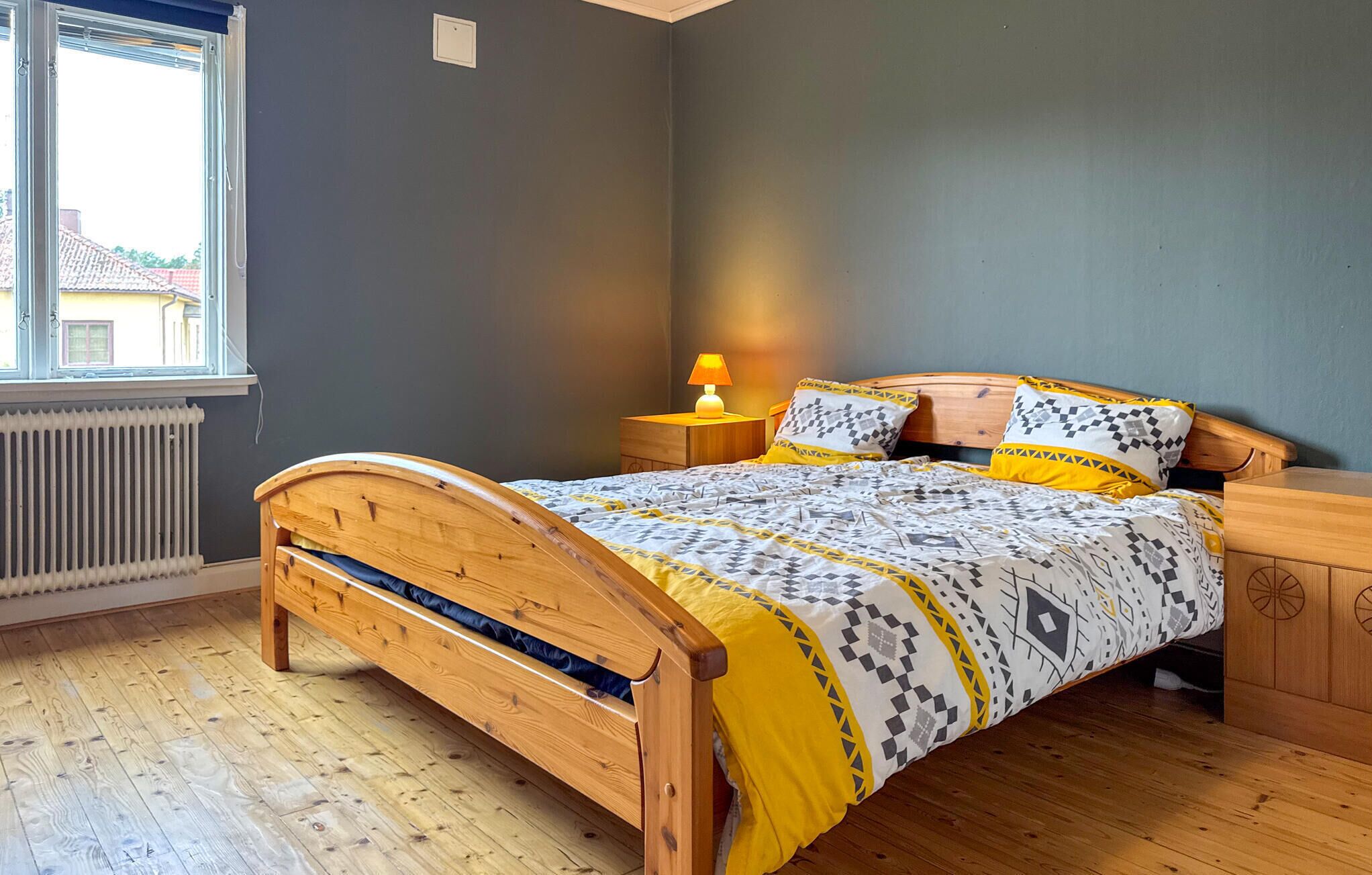 Un dormitorio con una cama de madera, una mesita de noche con una lámpara y un radiador.