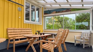An outdoor seating area with wooden benches and chairs, a small table, and a large window offering a view of greenery. - 2 bedroom beautiful home in Påskallavik (Påskallavik)