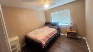 A bedroom with a bed, a ceiling fan, a window with blinds, and a nightstand with a lamp. - House with AC in Elk Grove (Elk Grove)