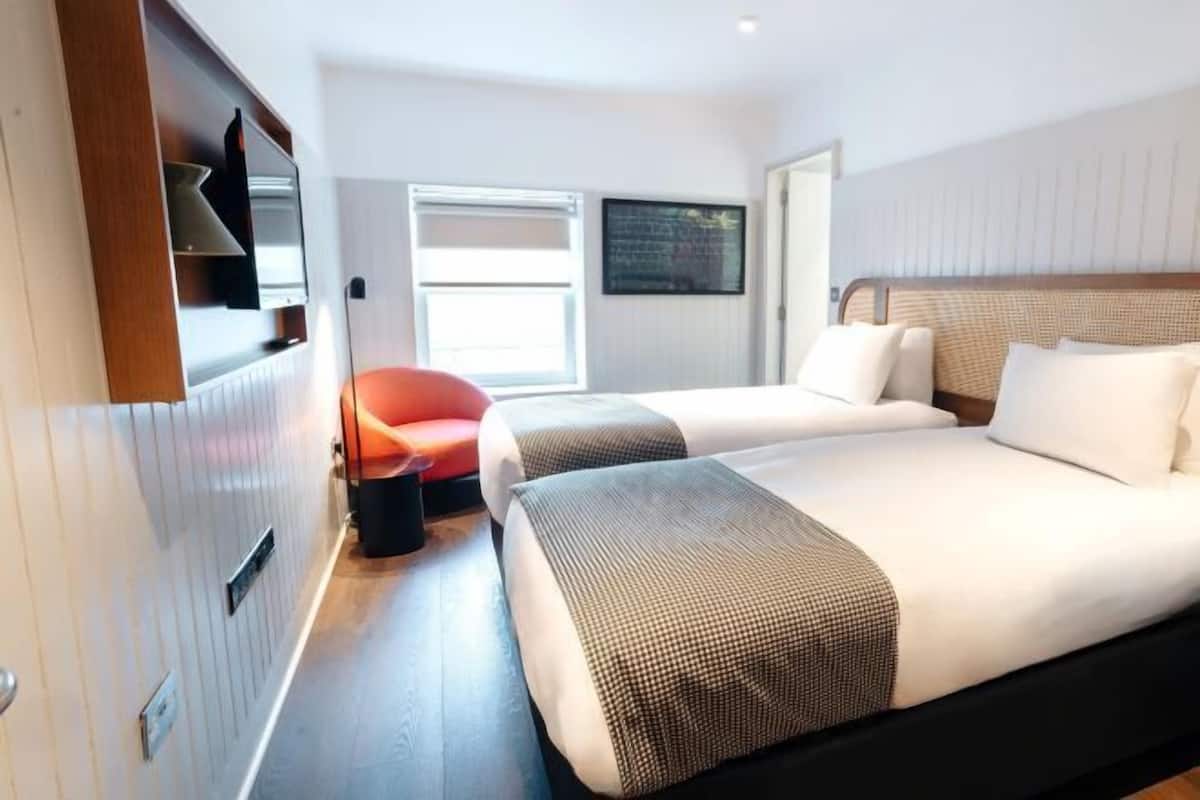 A hotel room with two beds, a TV mounted on the wall, a window, and a red chair.