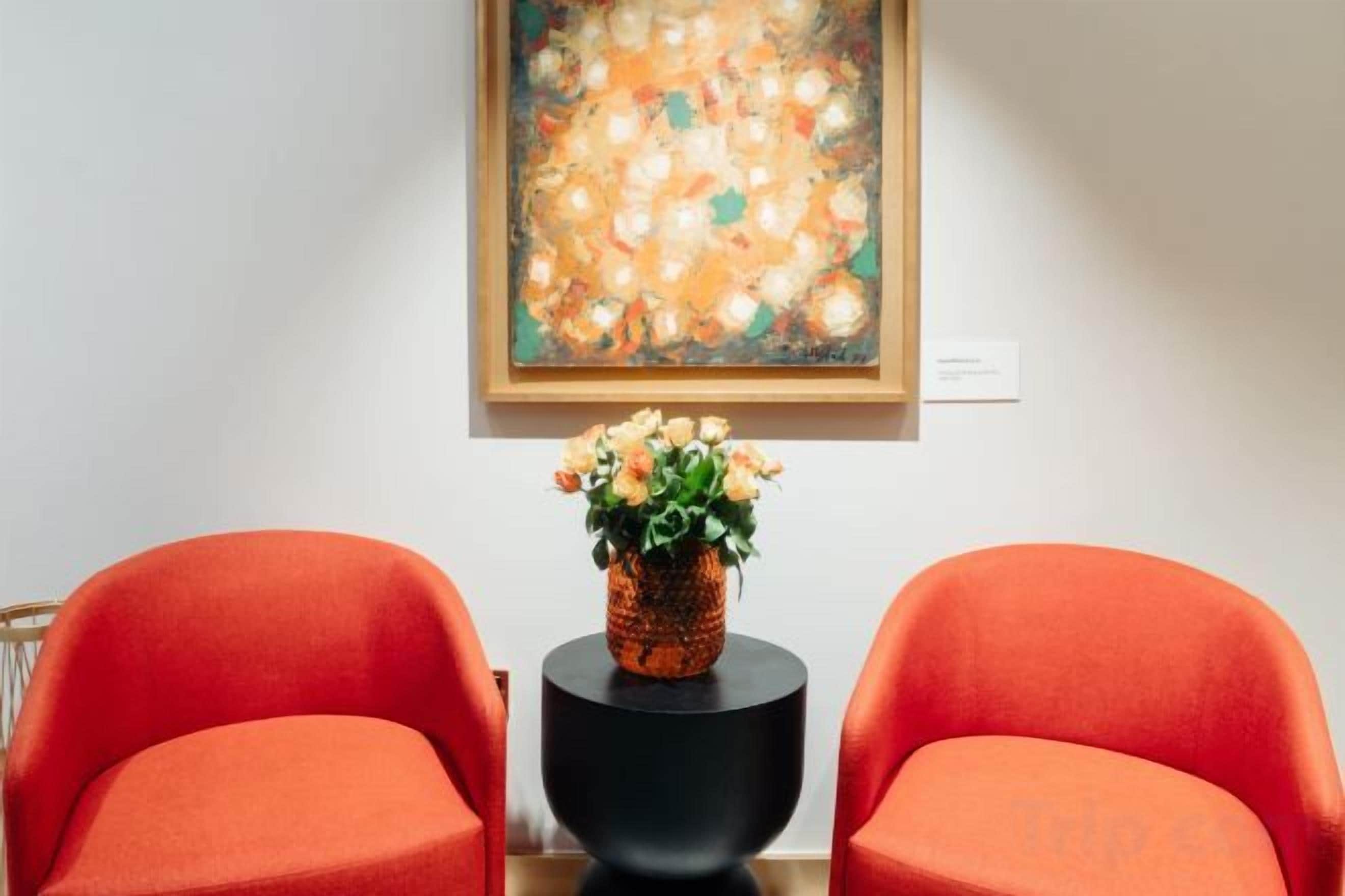 A room with two orange chairs, a black side table, and a painting on the wall.