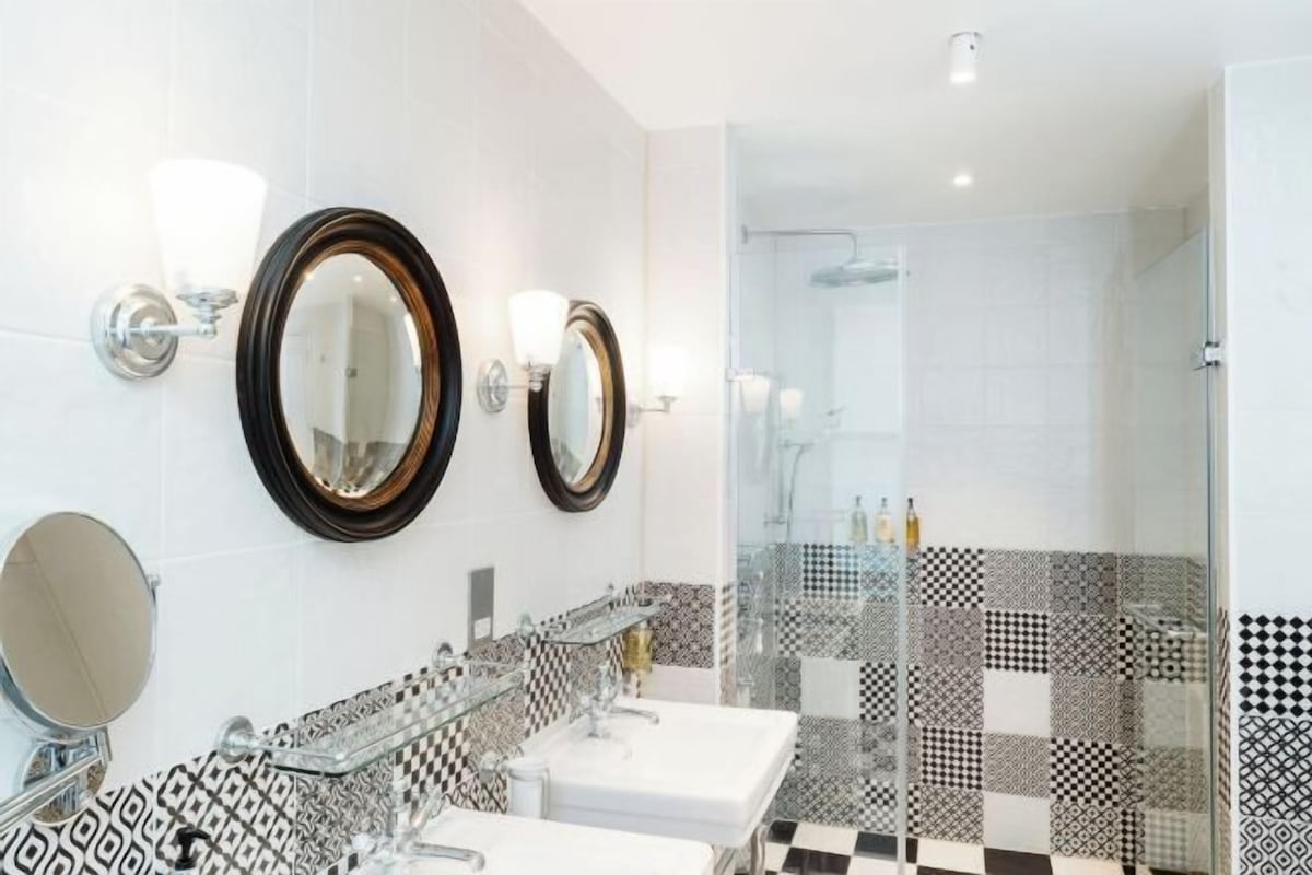 A modern bathroom with two sinks, a glass shower enclosure, and patterned tiles.