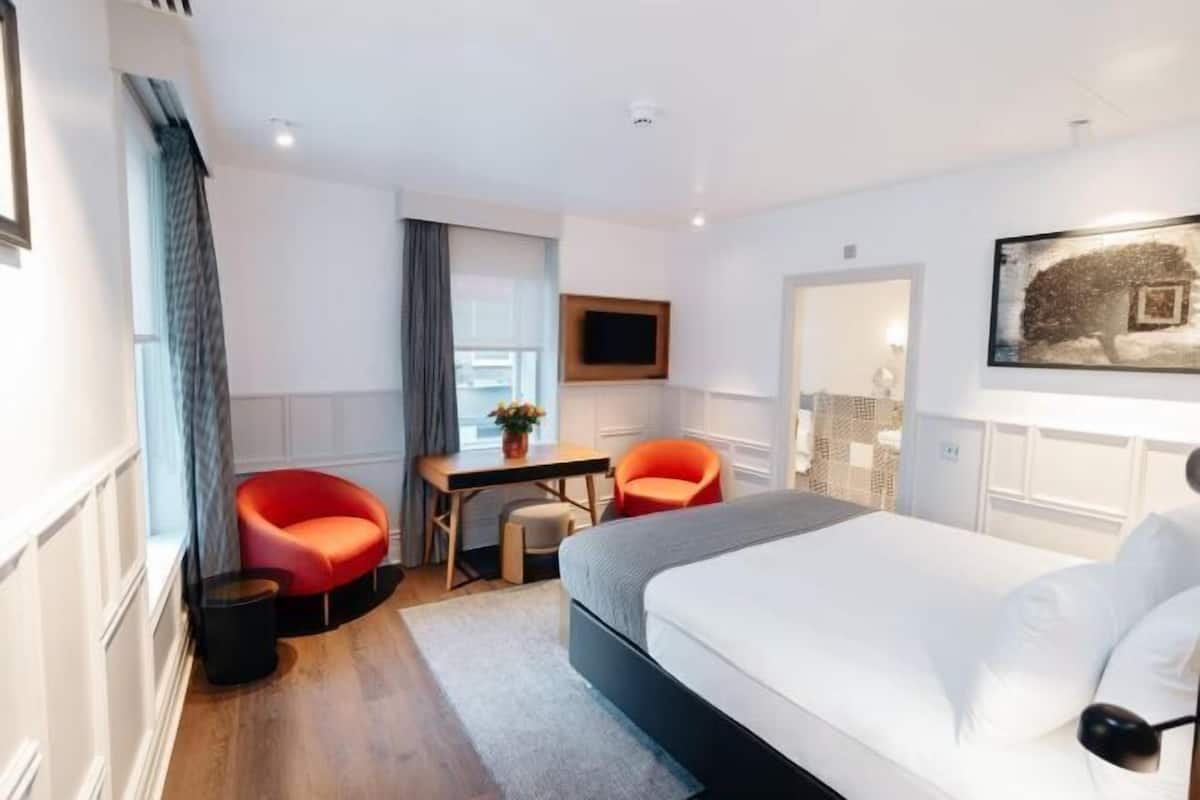 A modern hotel room with a bed, two chairs, a desk, and a TV.