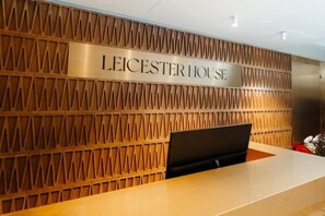 Een receptiebalie met een bord waarop 'LEICESTER HOUSE' staat, voor een wand met een patroon.