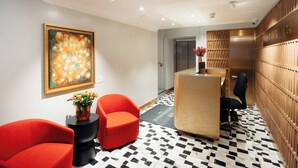 A modern reception area with a check-in counter, two red chairs, a painting, and a patterned floor. - Leicester House Hotel (London)