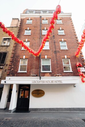 A hotel with a brick facade, a black entrance door, and a sign reading 'LEICESTER HOUSE HOTEL'. - Leicester House Hotel (London)