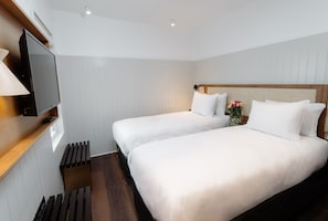 A hotel room with two beds, a TV on a wooden shelf, and a small window. - Leicester House Hotel (London)