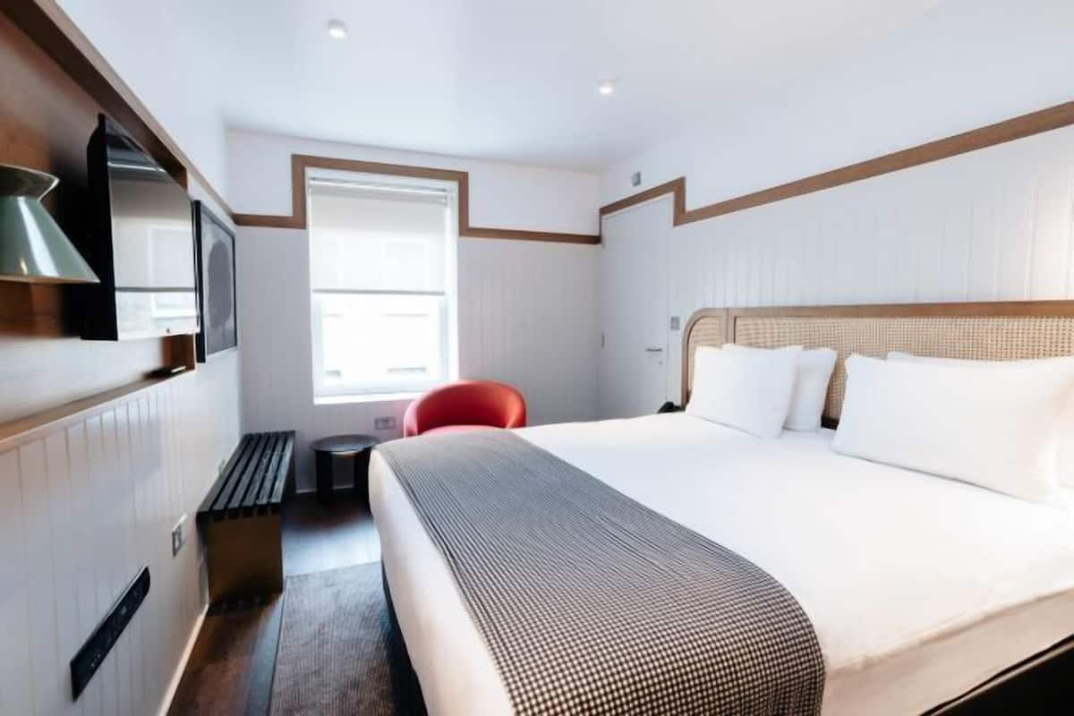 A hotel room with a bed, a television, a window, and a red chair.
