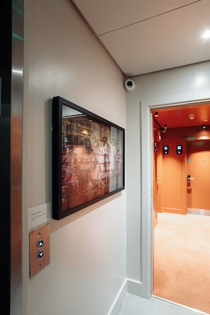 Un ascensor con pantalla digital, una cámara de seguridad en la pared y una obra de arte abstracta enmarcada.