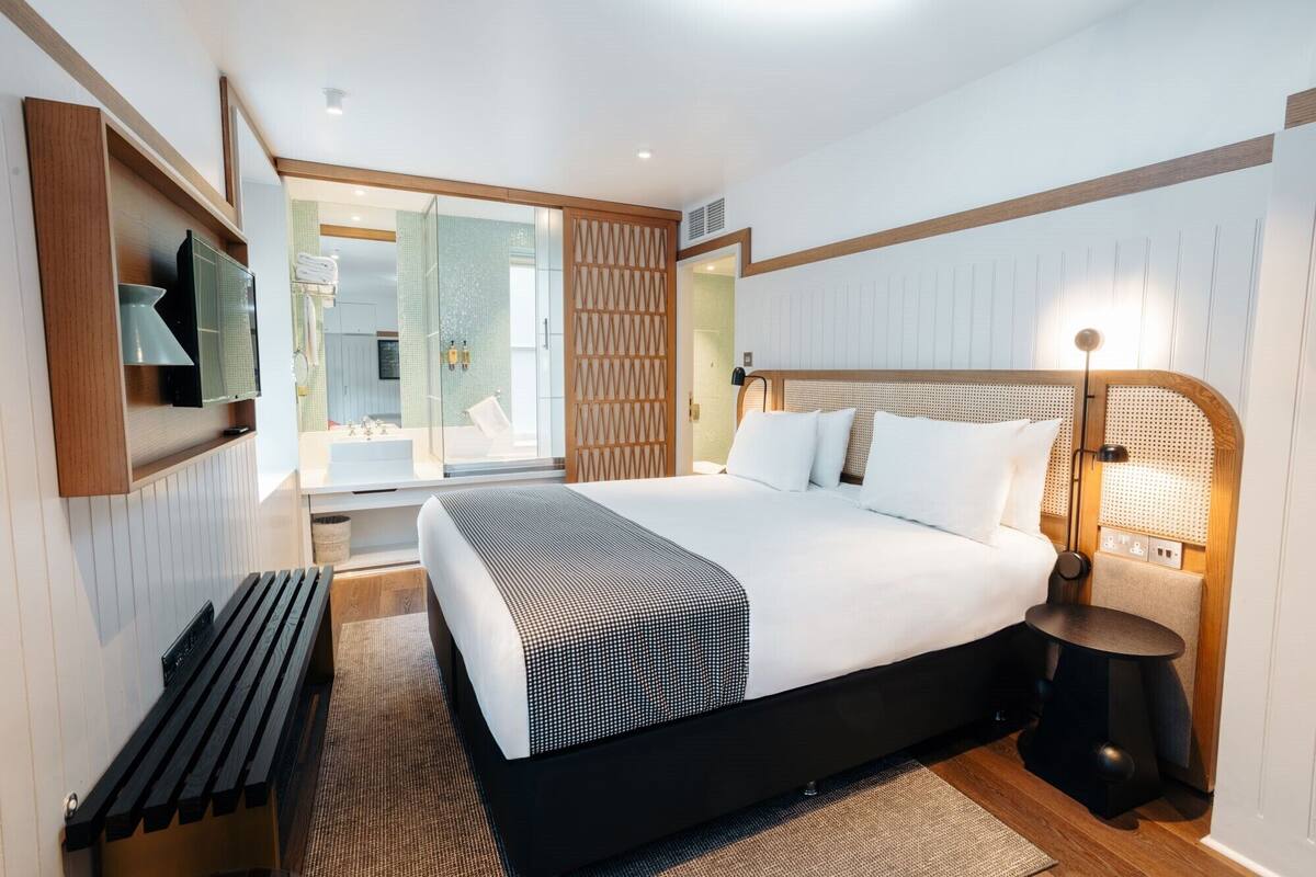 A modern bedroom with a large bed, a bedside table, a lamp, and a view of the bathroom.