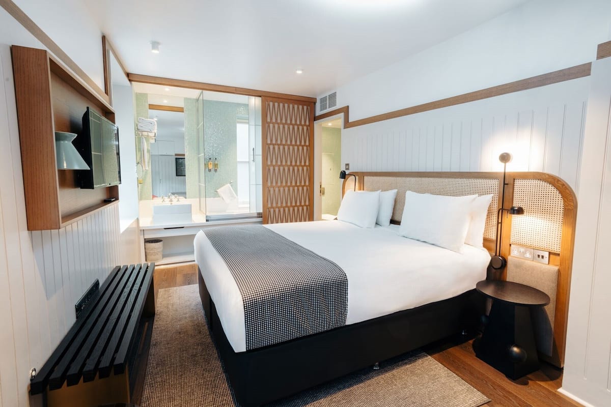 A modern hotel room with a large bed, a bedside table, a TV, and a window with a view.