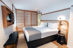 A modern hotel room with a large bed, a bedside table, a lamp, a TV, and a wooden partition. - Leicester House Hotel (London)