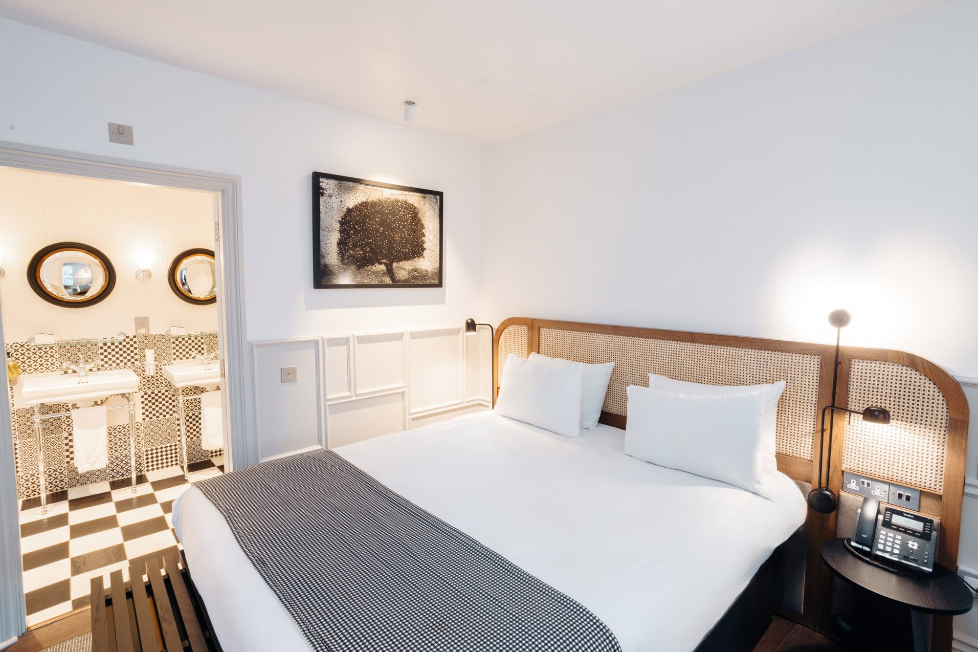 A hotel room with a bed, bedside table, and a wall-mounted picture.