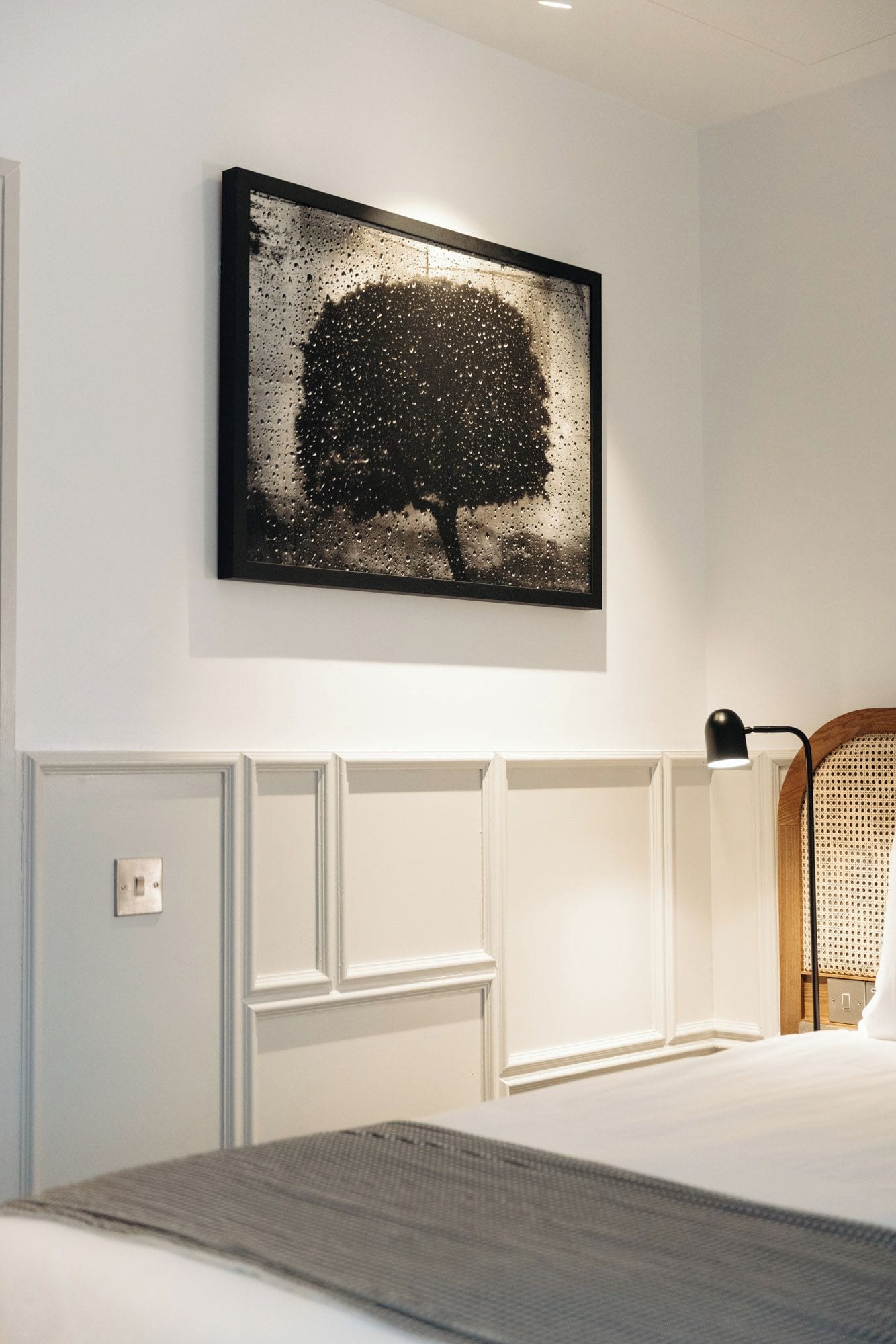 Une chambre à coucher avec un lit, un tableau accroché au mur, une lampe de chevet et un interrupteur.