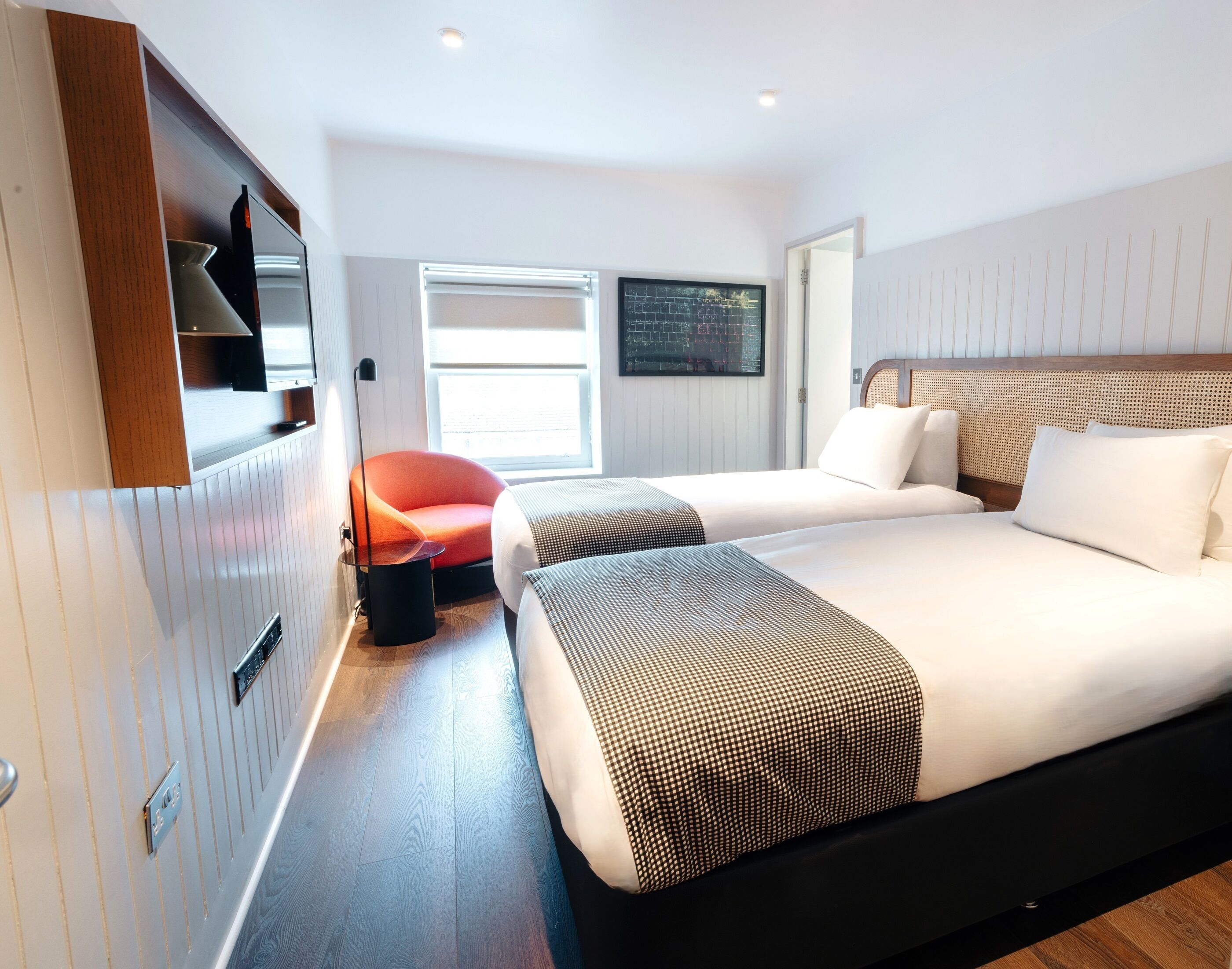 A modern hotel room with two beds, a TV, a window, and a door.