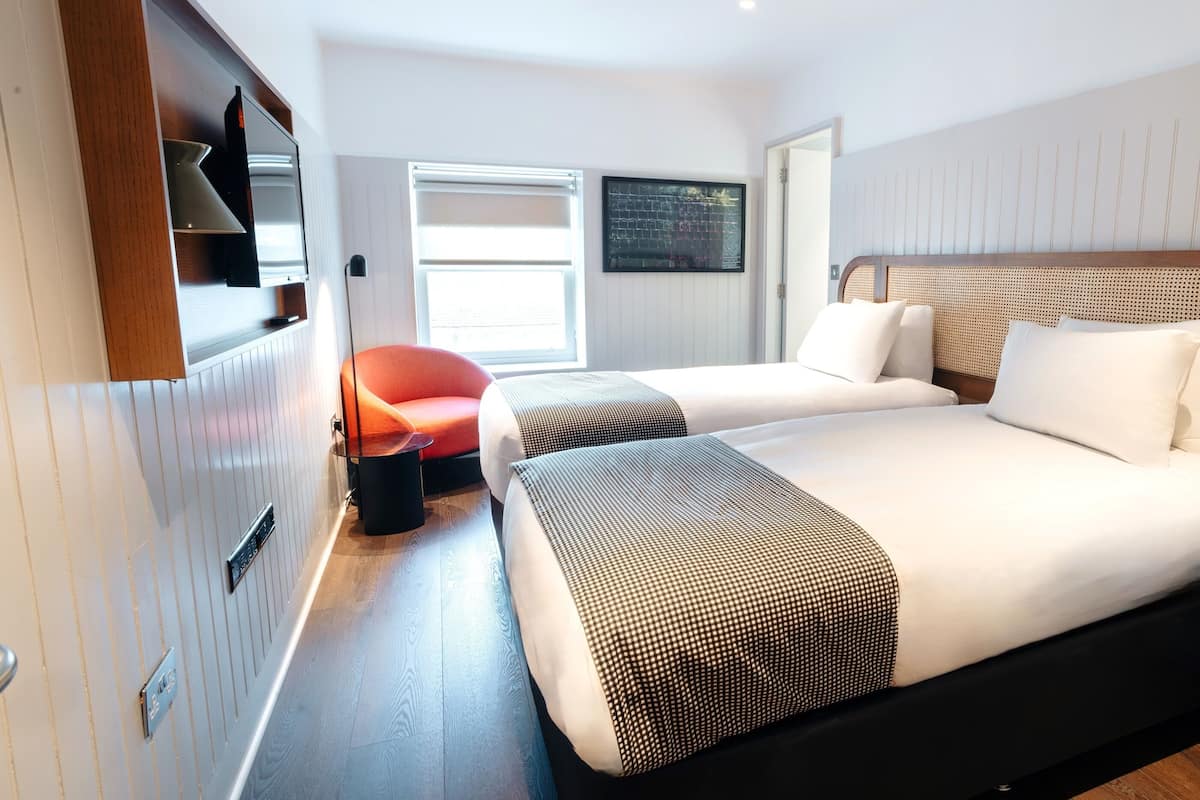 A modern hotel room with two beds, a TV, a window, and a door.