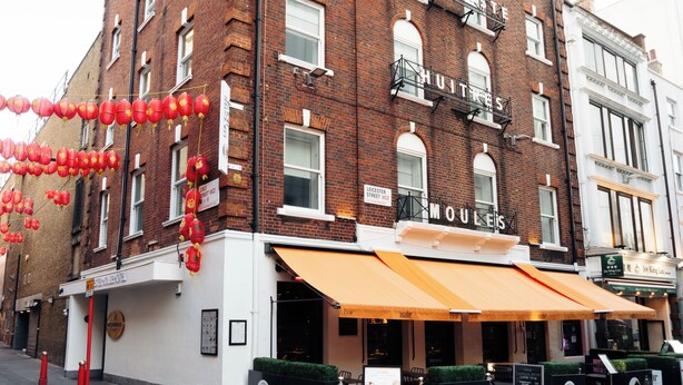 A brick building with 'Moules' signage, outdoor seating, and red lanterns. - Leicester House Hotel (London)