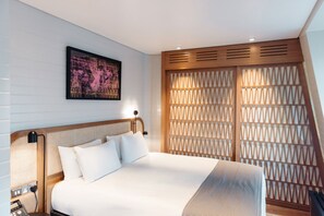 A modern bedroom with a large bed, a headboard with a woven design, a wall-mounted abstract painting, and a wooden partition with a geometric pattern. - Leicester House Hotel (London)