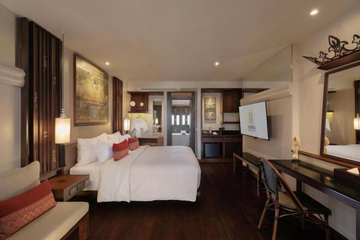 Habitación de hotel con cama, escritorio, silla, televisor y un espejo grande.