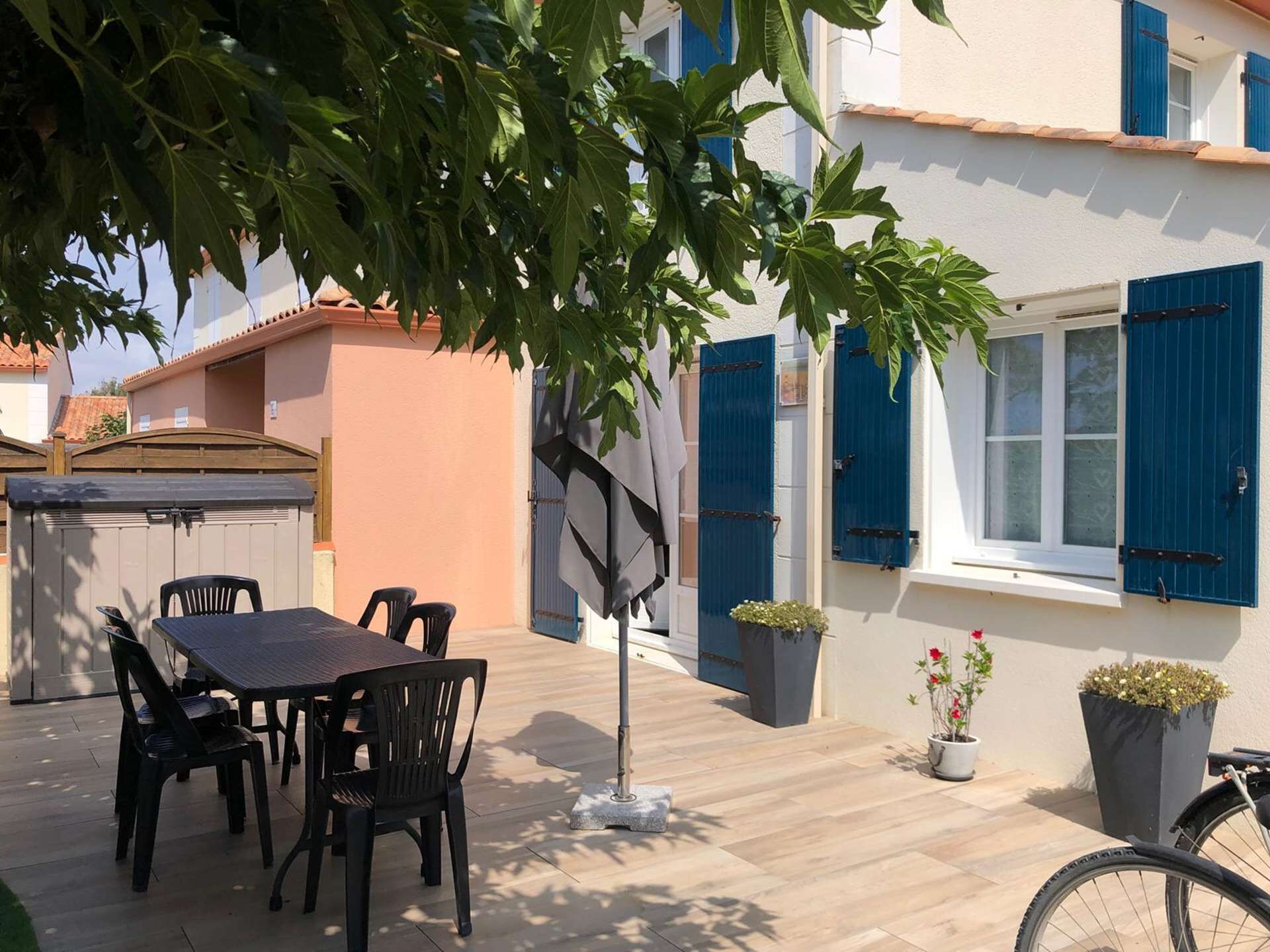An outdoor patio with a table and chairs, a tree, and potted plants.