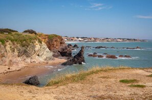 A coastal landscape with rocky formations, a sandy beach, and a distant town. - L’Oasis de la Parée Bretignolles (BRETIGNOLLES SUR MER)