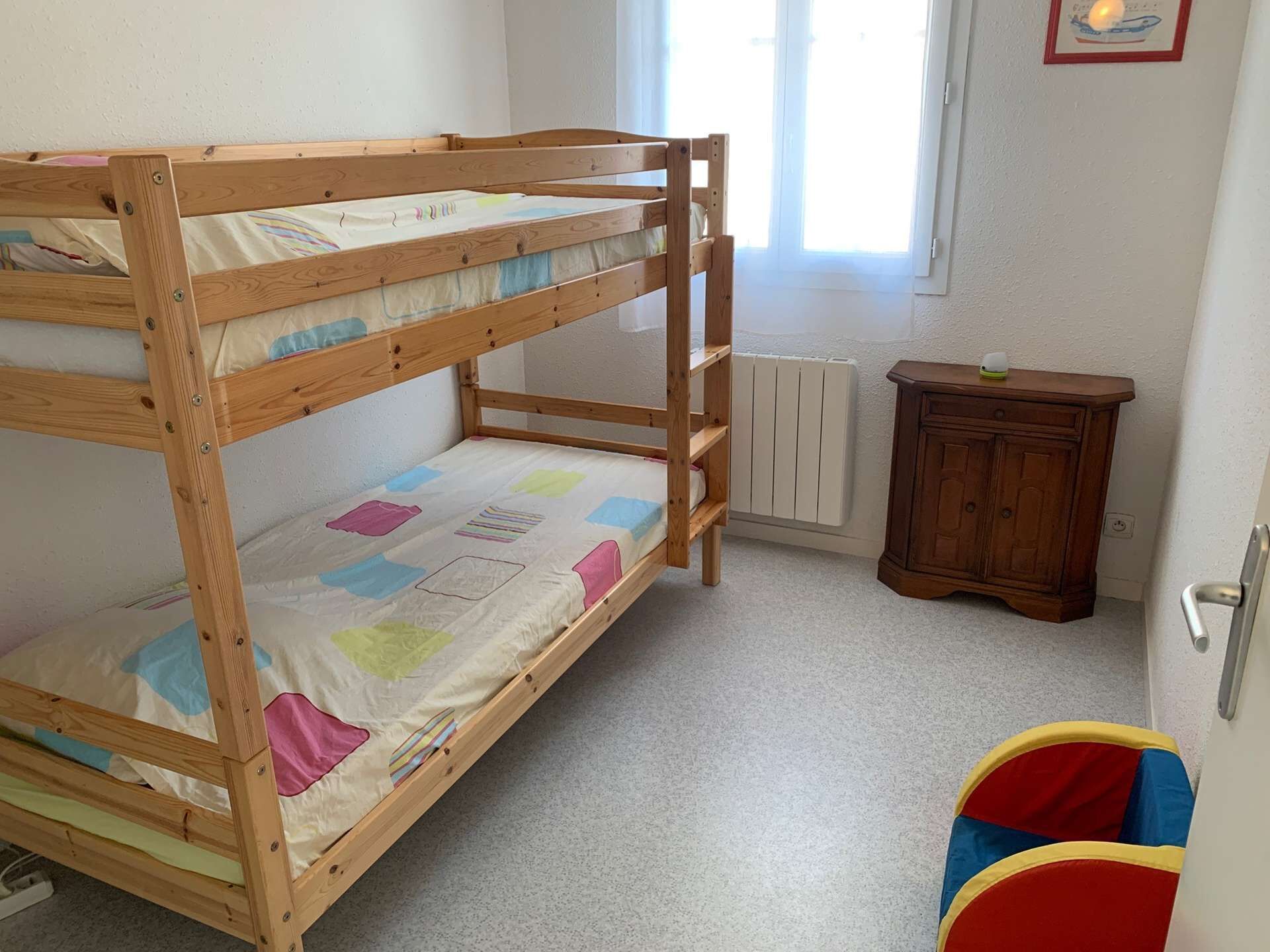 Ein Etagenbett mit Holzbettgestell, ein kleiner Schrank und ein bunter Spielbereich.