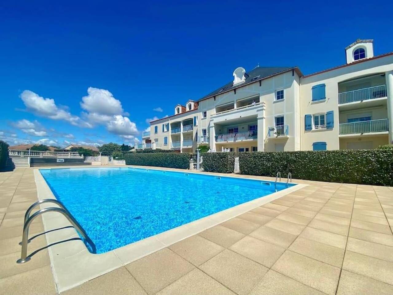 Piscina retangular com uma escada de metal de um lado, rodeada por um deck revestido de azulejos.