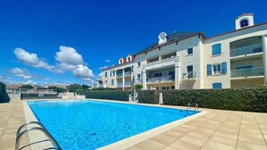 Et rektangulært swimmingpool med en metalstige på den ene side, omgivet af en fliseterrasse.