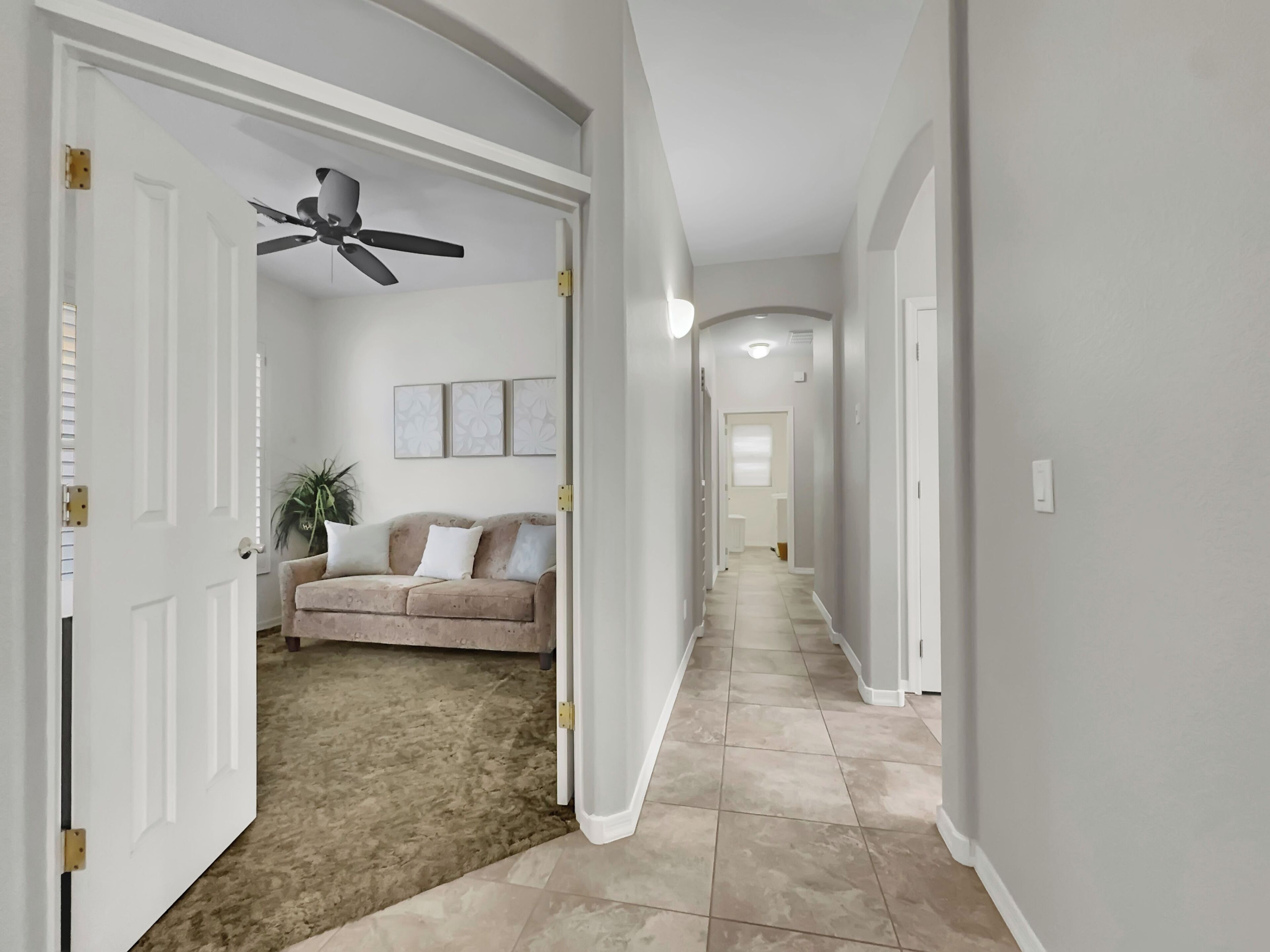 A hallway with a beige carpet, a ceiling fan, and a beige sofa with white cushions.