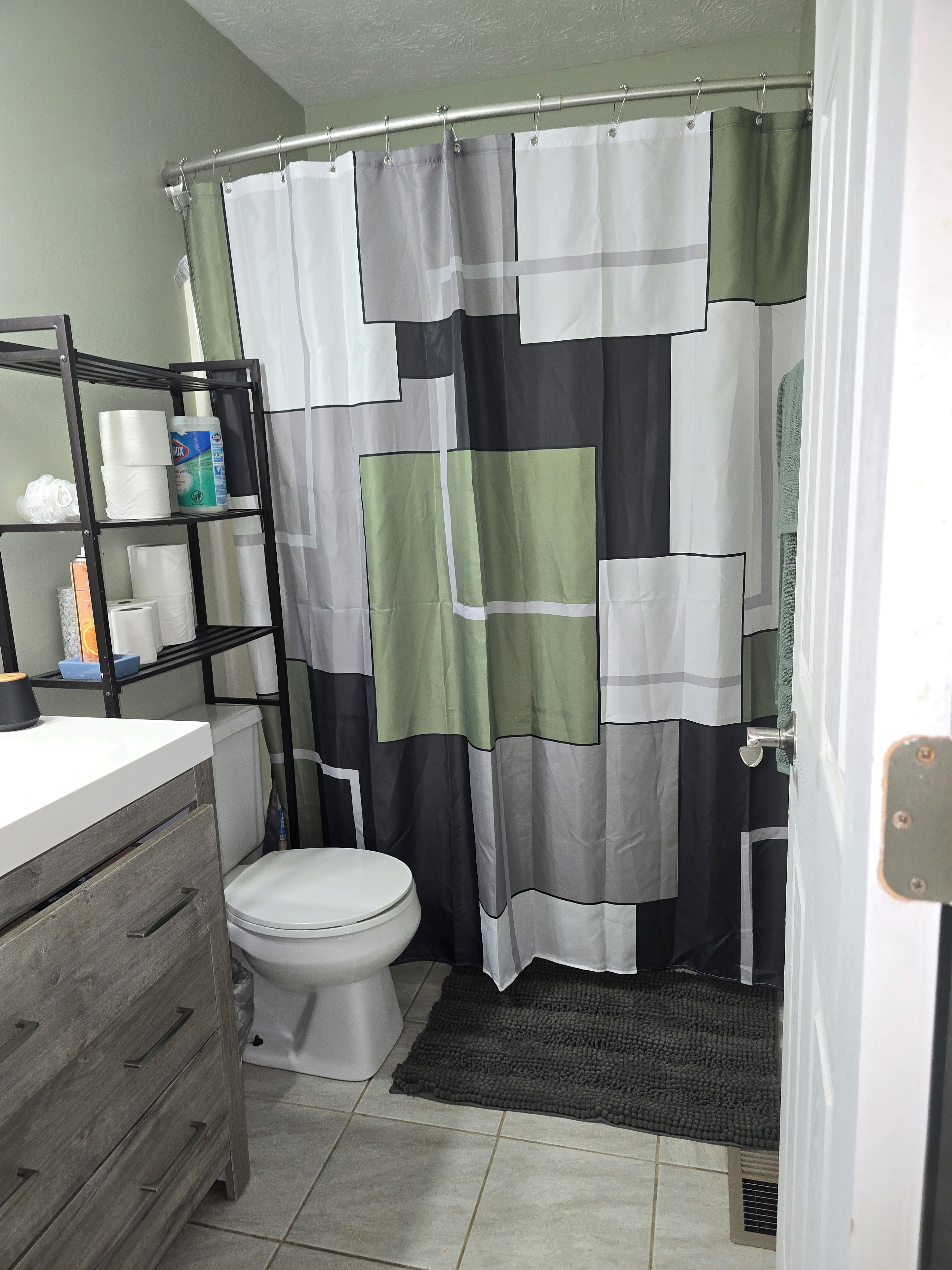 A bathroom with a shower curtain, toilet, and a shelf with toiletries.