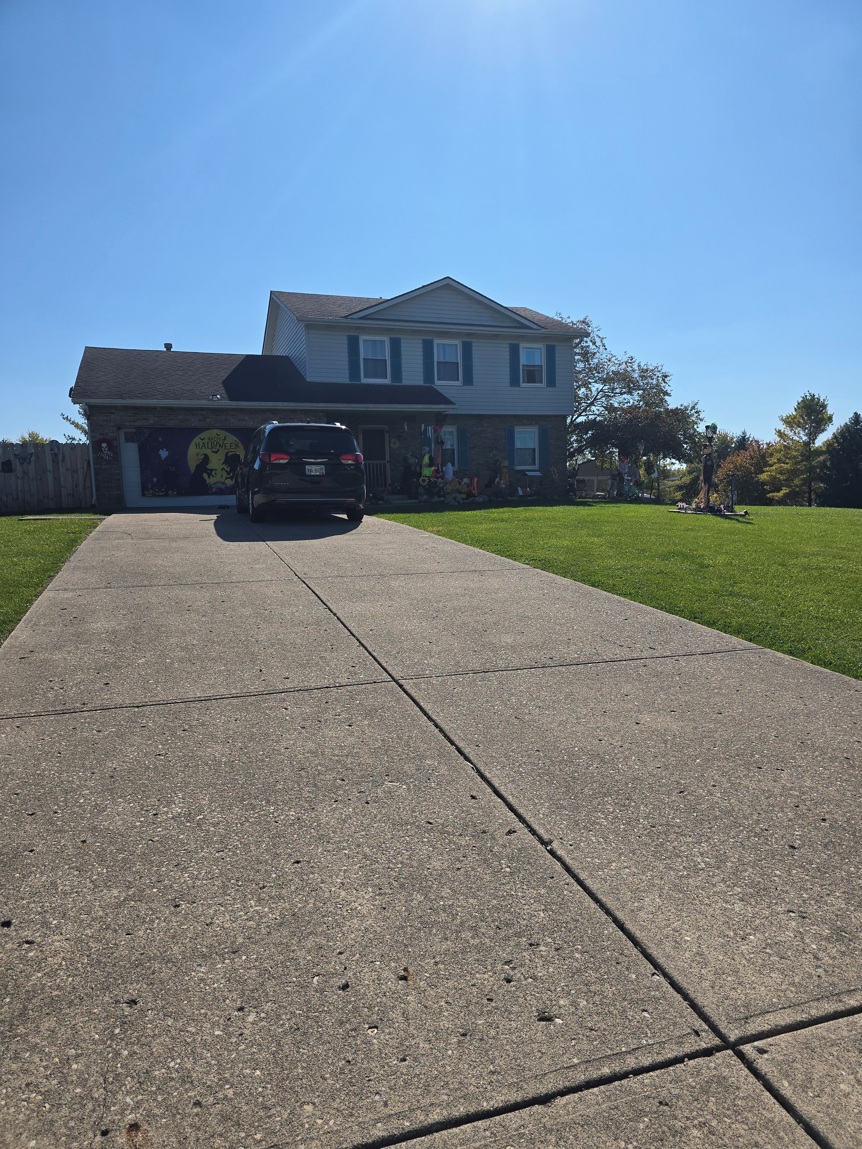 Une allée menant à une maison, avec un garage dont la porte est visible et un VUS garé devant.