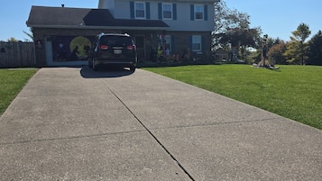Une allée menant à une maison, avec un garage dont la porte est visible et un VUS garé devant.