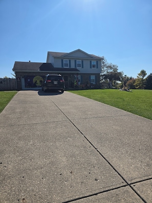 A residential driveway leading to a house with a visible garage door and a parked SUV.