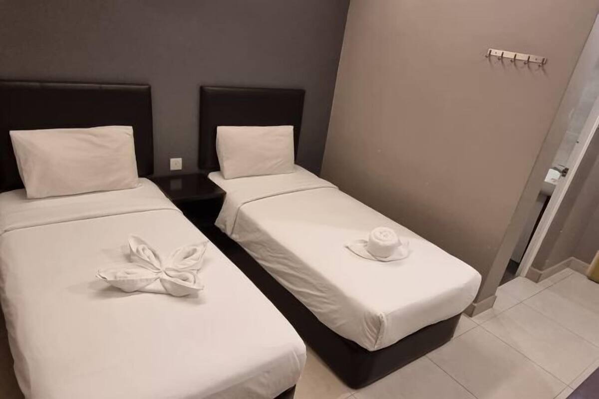 Habitación de hotel con dos camas individuales, cada una con una almohada y una toalla doblada con cuidado.