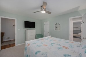 A bedroom with a bed, a ceiling fan, a TV, a dresser, and a door leading to a closet.